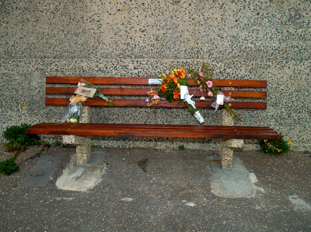 Wooden bench with bunches of flowers on and memorial plaque.