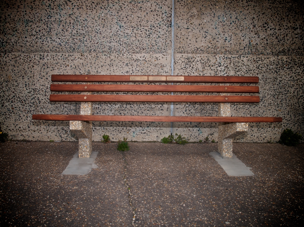 Wooden bench with three memorial plaques on.