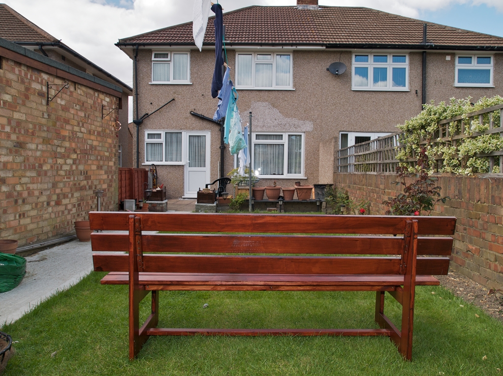 Wooden bench in on grass in back garden overlooking rear of house.