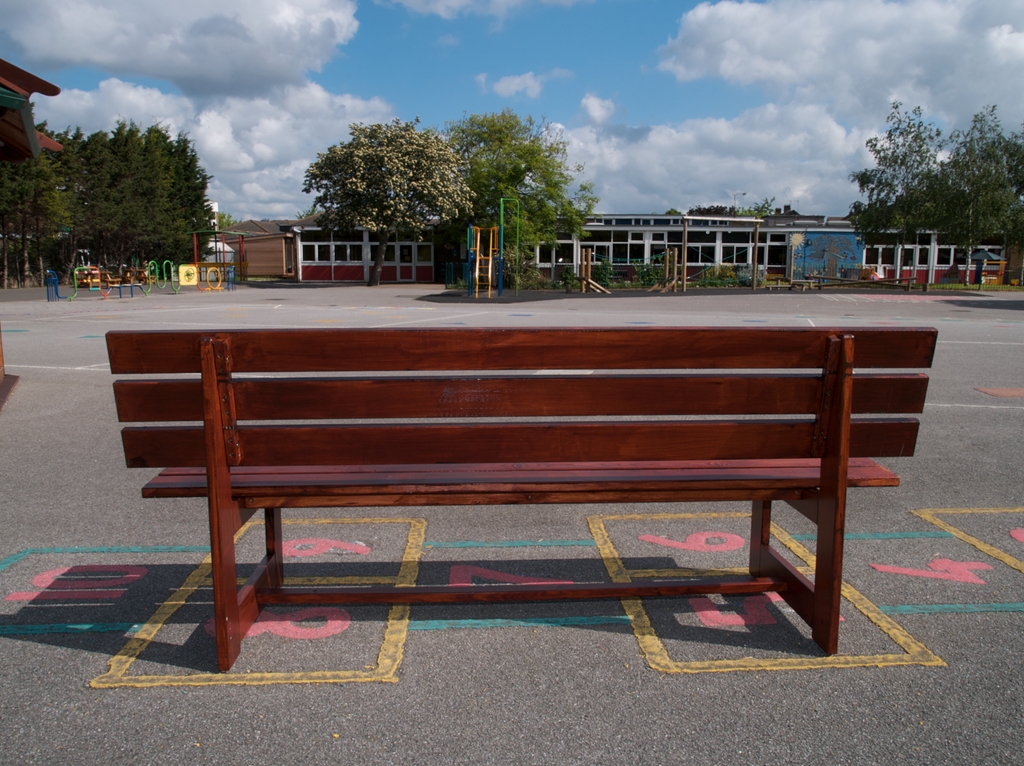 Wooden bench in primary school playground with school buildings in background.