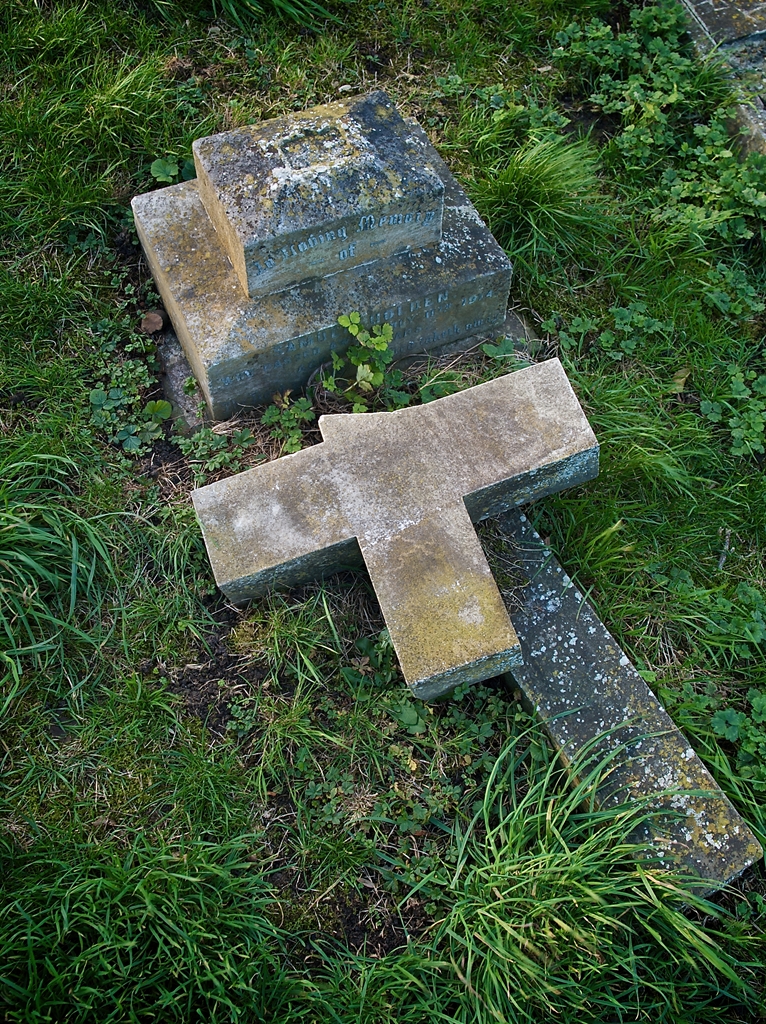 Old grave with broken headstone cross, untended and overgrown.